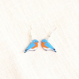 May include: A pair of bluebird earrings with silver hooks. The bluebirds are painted with blue, white, and orange details.