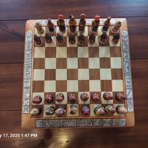 May include: A wooden chess set with intricately carved pieces and a checkered board. The pieces are painted with various colors and designs, and the board has decorative borders. The set is displayed on a dark wooden surface.
