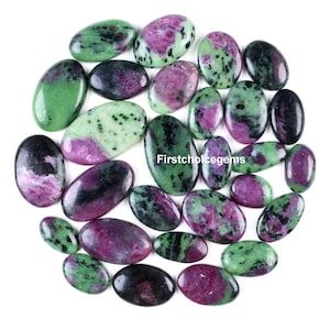 Puede incluir: Una colección de piedras preciosas ovaladas en tonos verdes, morados y negros. Las piedras preciosas están dispuestas en un patrón circular sobre un fondo blanco. El texto "Firstchoicegems" es visible en algunas piedras.