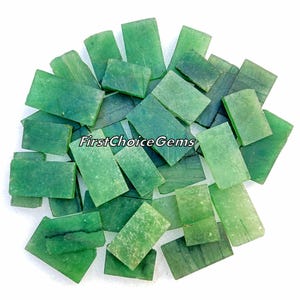 May include: A pile of green jade cabochons, cut into rectangular shapes. The stones are translucent and have a slight shimmer. The cabochons are perfect for jewellery making or other craft projects.