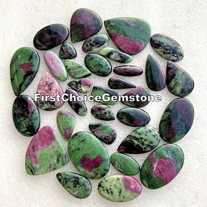 Puede incluir: Una colección de 25 cabujones de piedras preciosas verdes, negras y rosas. Las piedras son de diferentes formas y tamaños, y tienen una variedad de patrones. Las piedras están dispuestas en un círculo sobre un fondo blanco.