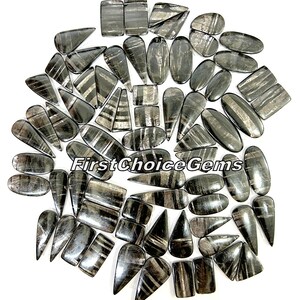 Puede incluir: Una colección de 40 cabujones de piedra preciosa rayados en negro y plata en varias formas, incluyendo oval, lágrima y rectangular. Las piedras están dispuestas en un círculo sobre un fondo blanco.