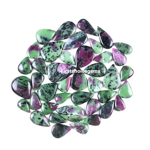 May include: A collection of polished ruby zoisite gemstones in various teardrop and oval shapes. The stones display a mix of green, black, and deep red hues. The text "firstchoicegems" is visible on the stones.