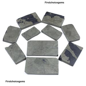 May include: A collection of rectangular pyrite stones, arranged in a circular pattern. The stones have a metallic gray color with dark, irregular patterns. The image includes the text "Firstchoicegems".