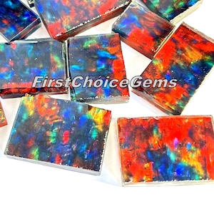 Può includere: Primo piano di diversi cabochon di opale iridescente, con una varietà di colori tra cui rosso, arancione, giallo, verde, blu e viola. I cabochon sono tagliati in forma rettangolare e hanno una superficie liscia e lucida. Il testo "FirstChoiceGems" è visibile nell'immagine.