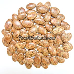 May include: A collection of 50 oval-shaped, brown and beige jasper cabochons with a mottled pattern. The stones are approximately 2.5 cm long and 1.25 cm wide.
