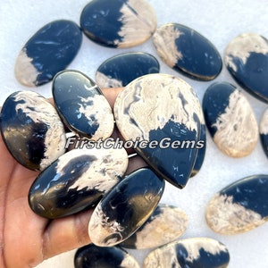 May include: A collection of polished gemstones in various oval and teardrop shapes. The stones feature a striking contrast of black and beige, with a marbled pattern. The text "FirstChoiceGems" is visible on the stones.