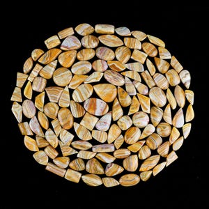 May include: A collection of yellow and white banded agate cabochons in various shapes and sizes. The cabochons are arranged in a circular pattern on a black background.