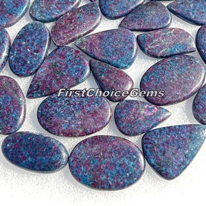 Może przedstawiać: Kolekcja niebieskich i fioletowych kaboszonów z kamieni szlachetnych w różnych kształtach kropli i owalnych. Kamienie mają nakrapiany wzór i są gotowe do oprawienia w biżuterię.