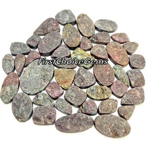 May include: A collection of 30 loose, natural, multi-colored, ruby gemstone cabochons. The cabochons are various shapes and sizes, with a rough, textured surface. The stones are a mix of pink, red, purple, and green hues.