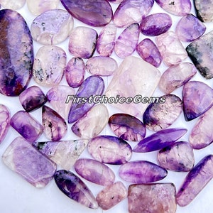 May include: A collection of 25 purple and white gemstone cabochons, with a variety of shapes and sizes. The cabochons are smooth and polished, with a natural, organic look.  FirstChoiceGems is printed on the image.