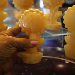 May include: A collection of five small, hand-carved, yellow-orange, flower-shaped sculptures. The sculptures are made of a translucent material, possibly alabaster or calcite. The sculptures are arranged on a table with a dark, starry surface.