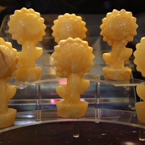 May include: Six small, hand-carved, yellow-orange, alabaster sculptures of sunflowers. Each sculpture is about 4 inches tall and features a detailed sunflower head and stem.