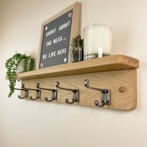 May include: A wooden shelf with five hooks and a small sign that reads "Sorry about the mess... We live here".