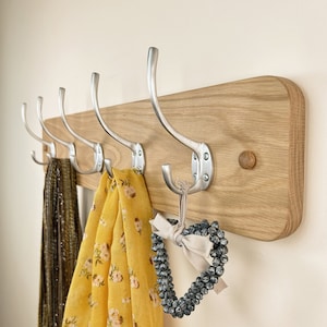 May include: A wooden wall-mounted coat rack with five silver hooks. Two scarves and a beaded heart are hanging on the hooks.