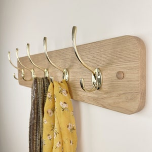 May include: A wooden coat rack with five brass hooks. Two scarves are hanging on the hooks.
