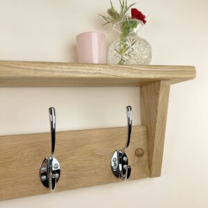 May include: A wooden shelf with two chrome hooks, a pink glass candle holder, and a clear glass vase with red and green flowers.