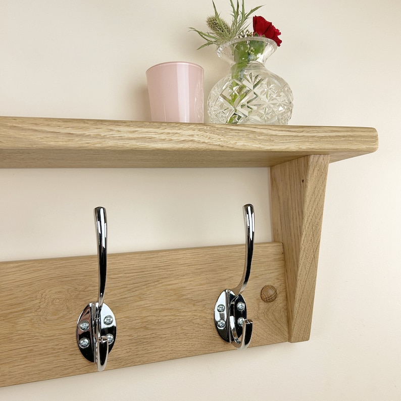 May include: A wooden shelf with two chrome hooks, a pink glass candle holder, and a clear glass vase with red and green flowers.
