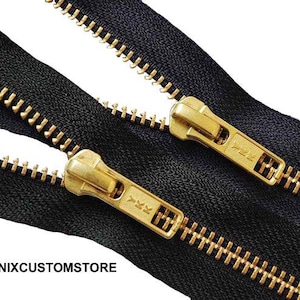 May include: Close-up of black zippers with gold-colored metal teeth and pulls. The zipper pulls have the text "YKK" on them. The zippers are on a white background. The logo "PHOENIXCUSTOMSTORE" is in the bottom left corner.