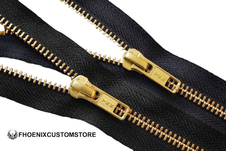May include: Close-up of black zippers with gold-colored metal teeth and pulls. The zipper pulls have the text "YKK" on them. The zippers are on a white background. The logo "PHOENIXCUSTOMSTORE" is in the bottom left corner.