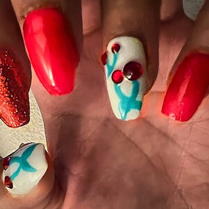 May include: Close-up of a hand with five red and white painted fingernails. The nails are decorated with glitter, red and white dots, and a turquoise design.
