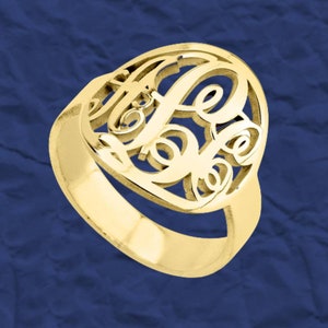K&ouml;nnte beinhalten: Ein goldener Ring mit einem Monogramm-Design. Der Ring ist aus einem einzigen St&uuml;ck Metall gefertigt und hat eine glatte, polierte Oberfl&auml;che.