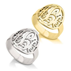 K&ouml;nnte beinhalten: Zwei Monogram Ringe, einer in Silber und einer in Gold, mit einem herzf&ouml;rmigen Design mit einem Monogramm aus drei Buchstaben.