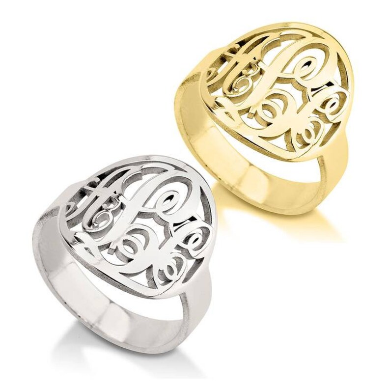 K&ouml;nnte beinhalten: Zwei Monogram Ringe, einer in Silber und einer in Gold, mit einem herzf&ouml;rmigen Design mit einem Monogramm aus drei Buchstaben.