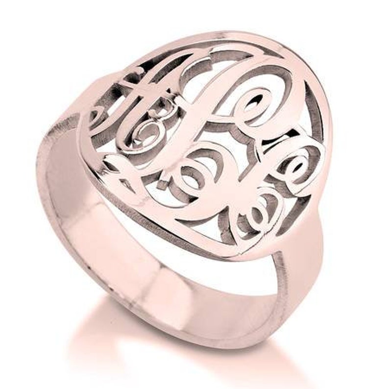 K&ouml;nnte beinhalten: Ein Ring aus Ros&eacute;gold mit einem Monogramm-Design. Der Ring ist aus Metall und hat eine glatte Oberfl&auml;che.