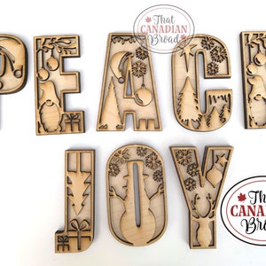 May include: Wooden cutout letters spelling "PEACE JOY" with various Christmas-themed designs inside each letter. The letters are on a white background.