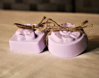 May include: Two lavender-coloured soap bars with a floral design, tied together with twine.