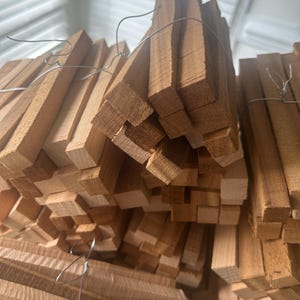 May include: A stack of rectangular wooden pieces, tightly bound with silver wire. The wood has a natural, light brown color and a visible grain. The pieces are uniform in size and shape, suggesting they are for a specific craft or construction project.
