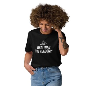May include: A black t-shirt with white text that reads "What was the reason?!" The shirt features a small graphic of a hand holding a magnifying glass. A person is wearing the shirt and blue jeans.