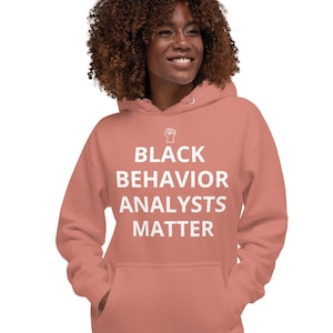 May include: A coral pink hoodie with a white raised fist and the text "BLACK BEHAVIOR ANALYSTS MATTER" printed on the front.