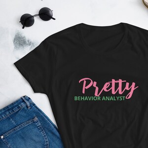 May include: Black t-shirt with the text "Pretty Behavior Analyst" in pink and green lettering.
