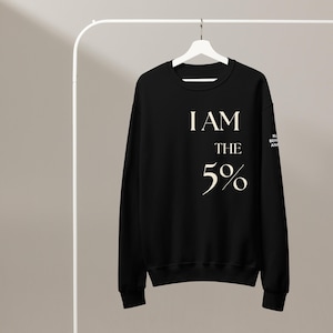 May include: Black crew neck sweatshirt with the text "I AM THE 5%" in a cream color. The sweatshirt is hanging on a white hanger. The sleeve has the text "BL BEHAVIOR ANAL".