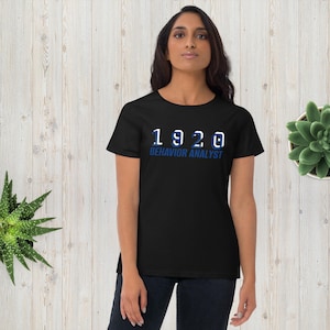 May include: Black t-shirt with white text that reads "1920 BEHAVIOR ANALYST" in a blue outline.