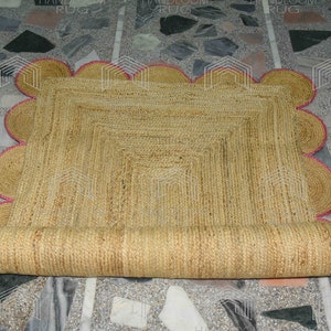 May include: A natural fiber rug with a scalloped edge and a pink trim. The rug is rolled up and has a natural, woven texture.