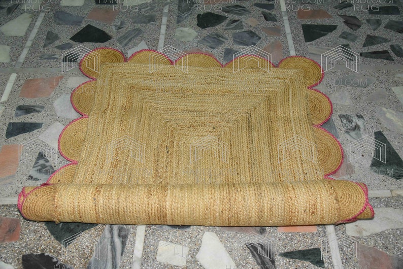 May include: A natural fiber rug with a scalloped edge and a pink trim. The rug is rolled up and has a natural, woven texture.