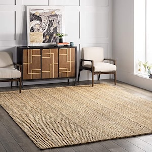 May include: A natural fiber rug in a light brown color with a woven texture. The rug is placed in a living room setting with two chairs and a cabinet.