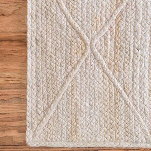 May include: A close-up of a white braided rug with a diamond pattern. The rug is made of natural fibers and has a textured surface.