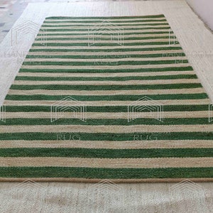 Op de afbeelding: Een gestreept jute vloerkleed met groene en natuurlijke gekleurde strepen. Het vloerkleed is gemaakt van natuurlijke vezels en heeft een rustieke uitstraling.