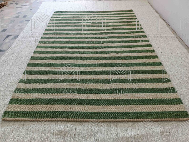 Op de afbeelding: Een gestreept jute vloerkleed met groene en natuurlijke gekleurde strepen. Het vloerkleed is gemaakt van natuurlijke vezels en heeft een rustieke uitstraling.