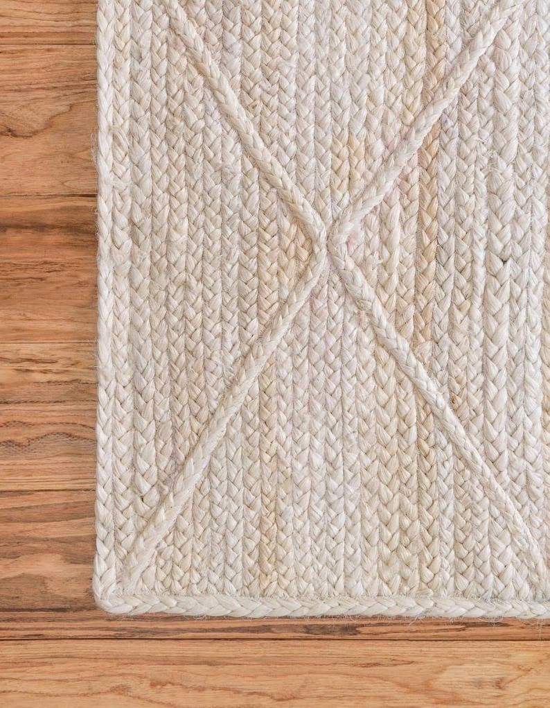 May include: A close-up of a white braided rug with a diamond pattern. The rug is made of natural fibers and has a textured surface.