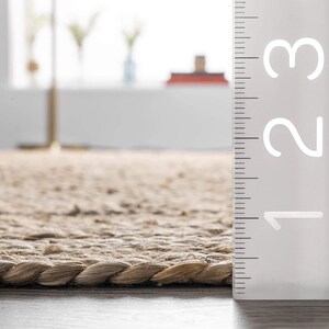 May include: Close-up of a natural fiber rug with a braided edge. A ruler is placed next to the rug, showing the measurement of 1, 2, and 3.