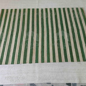 Op de afbeelding: Een groen en natuurlijk jute gestreept tapijt. Het tapijt is gemaakt van natuurlijke materialen en heeft een handgeweven uitstraling.