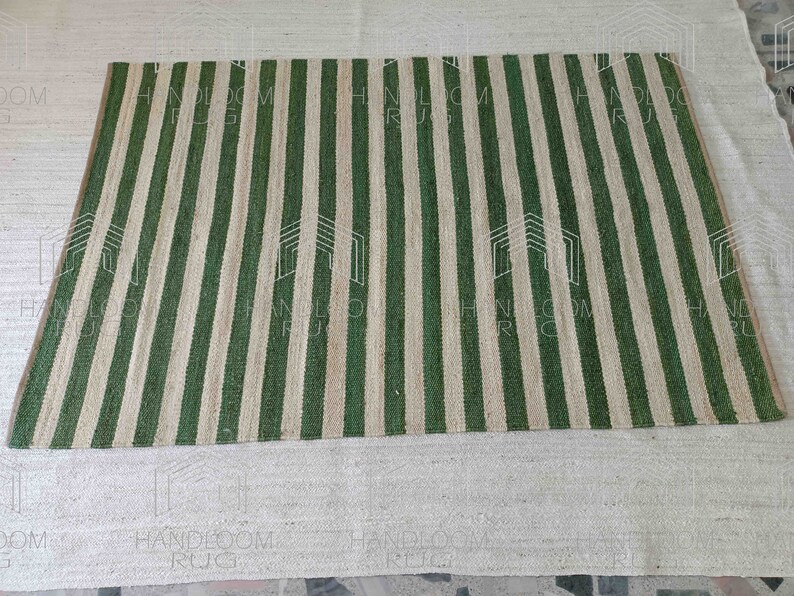 Op de afbeelding: Een groen en natuurlijk jute gestreept tapijt. Het tapijt is gemaakt van natuurlijke materialen en heeft een handgeweven uitstraling.