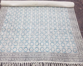 Könnte beinhalten: Ein weißer und blauer Teppich mit schwarzem Rand und Fransen. Der Teppich hat ein geometrisches Design mit einem floralen Motiv.