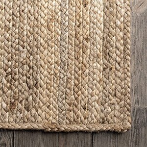 May include: A natural fiber rug made from woven jute. The rug has a braided texture and a natural beige color.