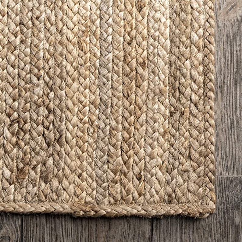 May include: A natural fiber rug made from woven jute. The rug has a braided texture and a natural beige color.